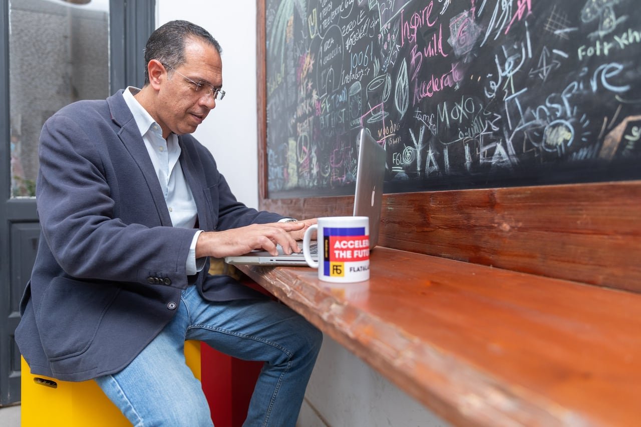A founder working at his laptop in front of a chalkboard wall.