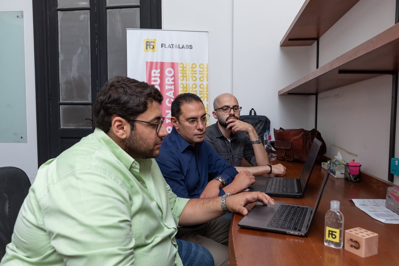 Three team members around a laptop at the Flat6Labs office.