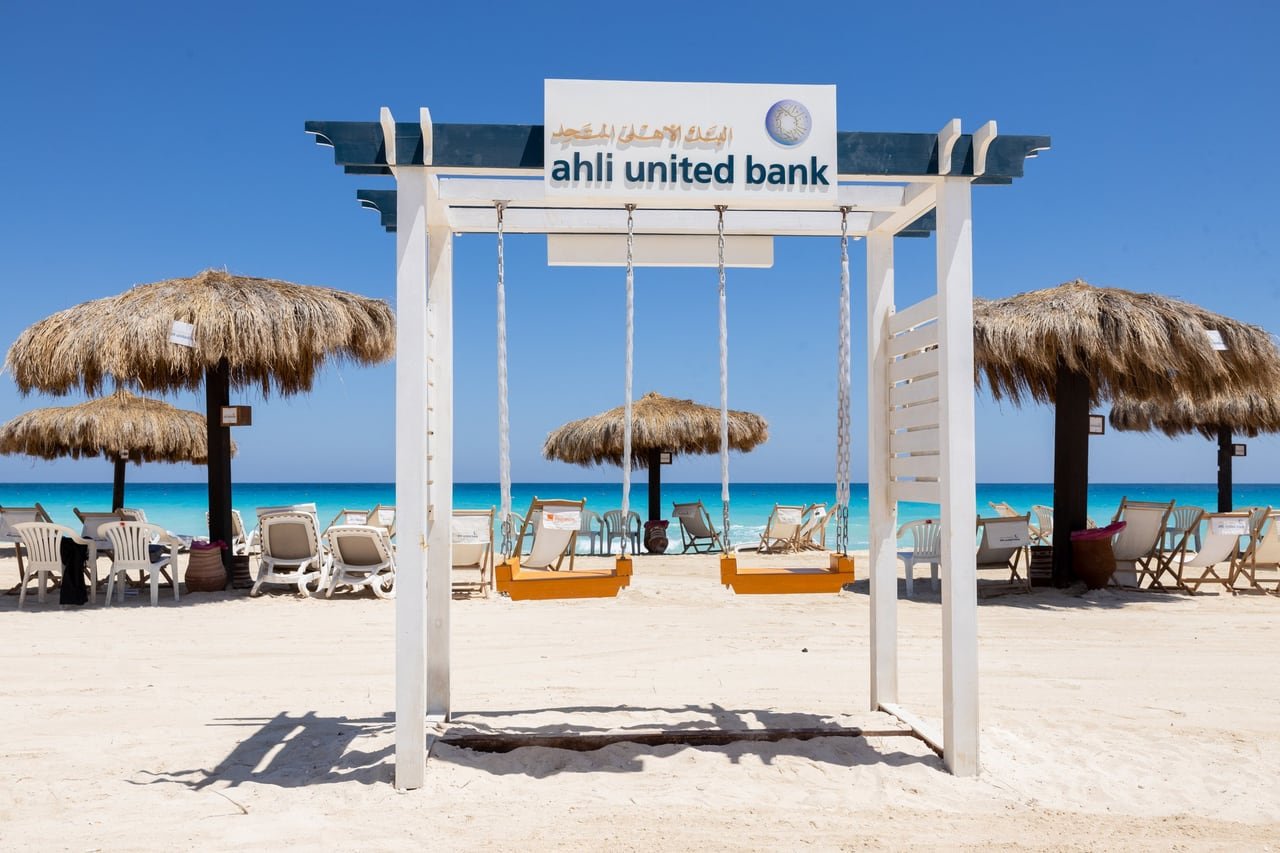 A branded swing on the beach, with the sea behind it.
