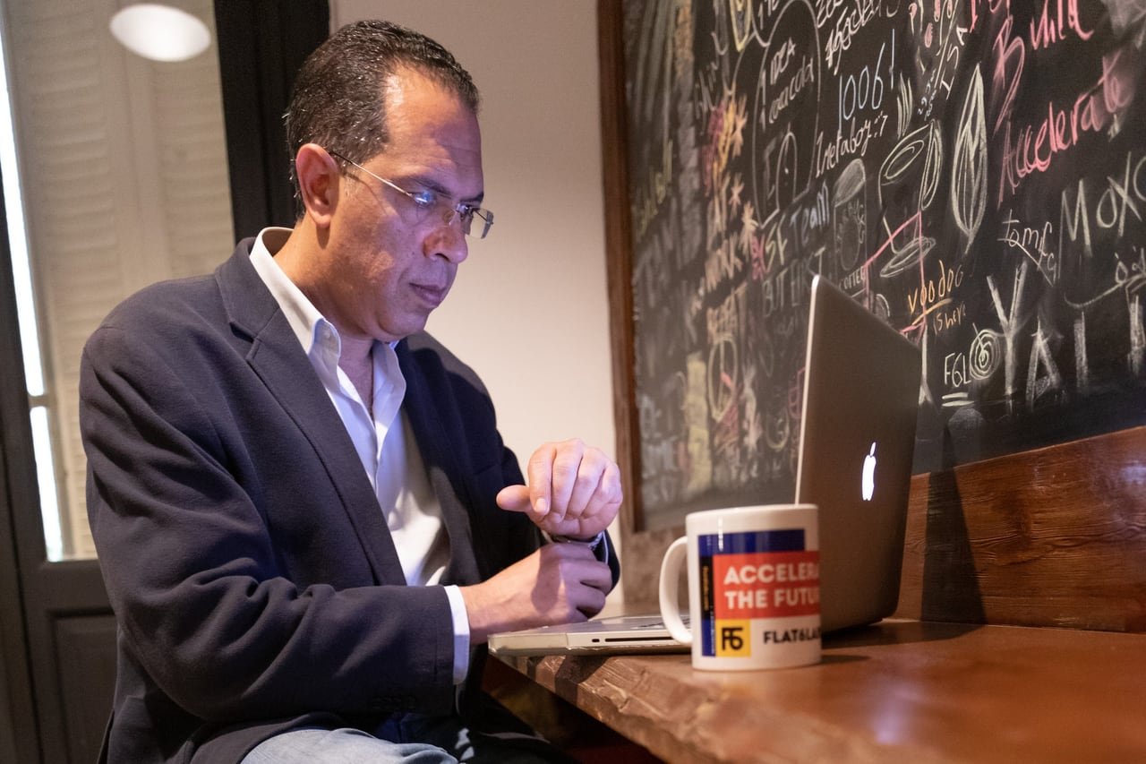 A close portrait of a founder at his desk, a Flat6Labs mug beside him.