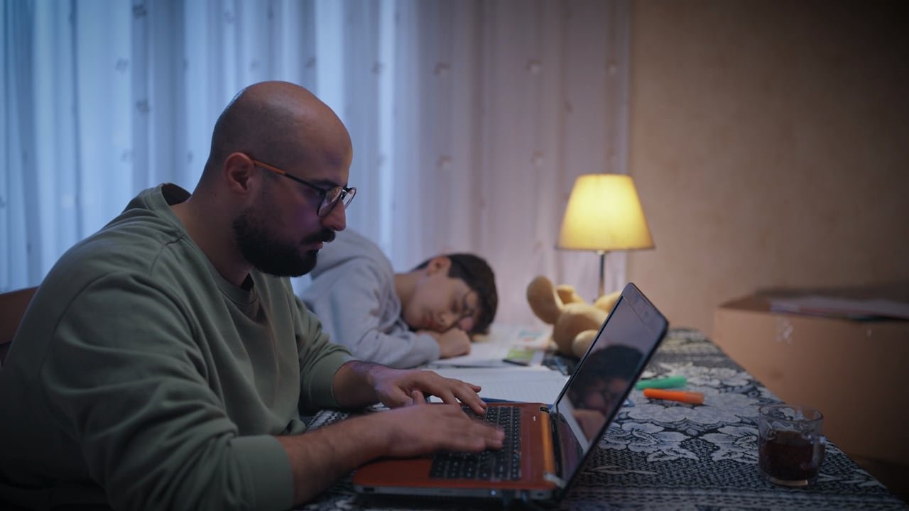 أب يعمل ليلًا على حاسوبه وابنته نائمة بجواره.