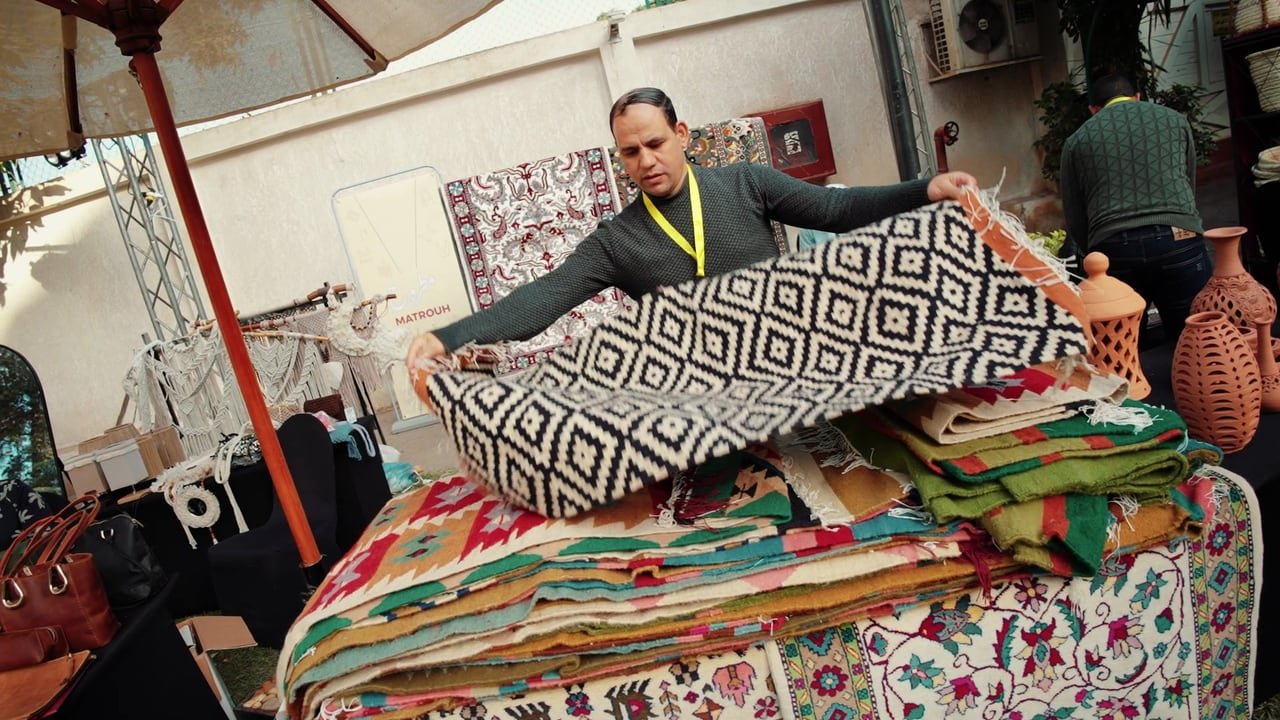 A craftsman unfolding a woven textile at his stall.