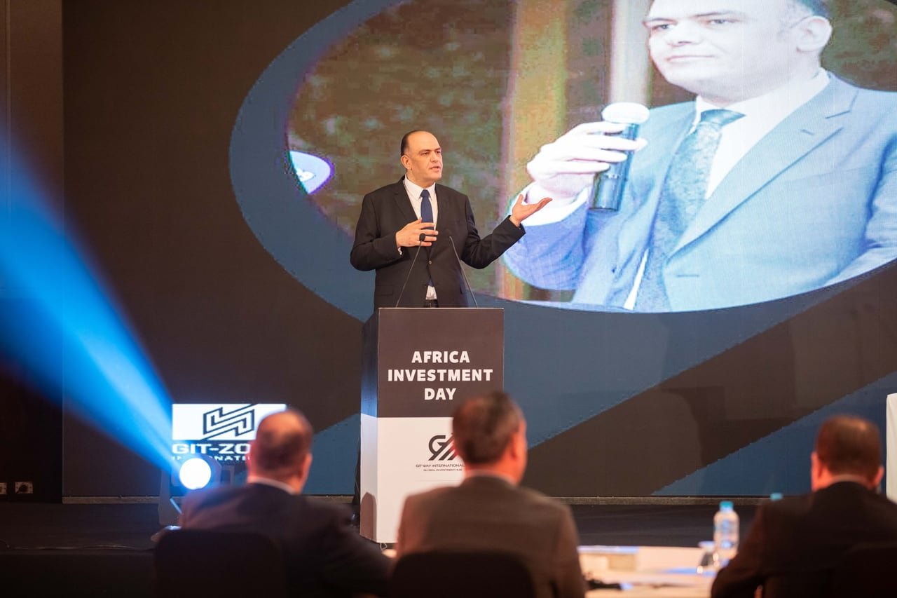A speaker at the Africa Investment Day podium, his image enlarged on the screen behind him.