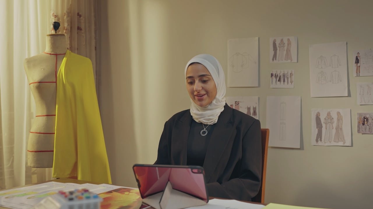 مصممة أزياء على حاسوبها بجوار مانيكان.