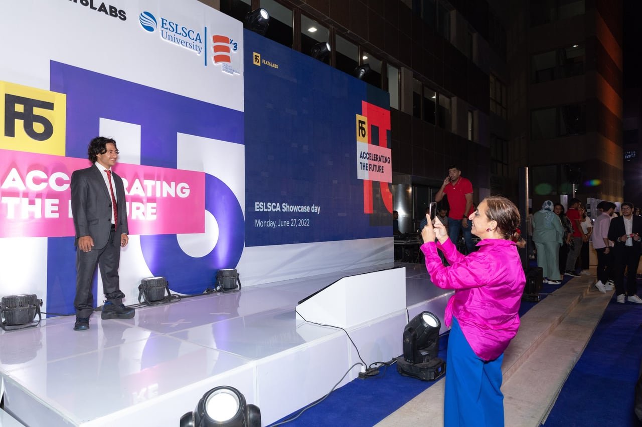 A guest filming a pitch on stage with her phone.