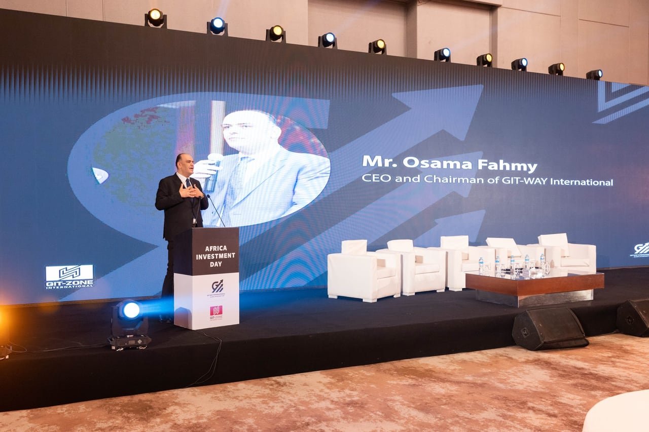 The wide LED stage and the white panel chairs during the opening speech.